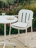 HAY Barro Plates, Pistachio, glazed portuguese terracotta plates, on a white garden table with an armchair and stem glass by flowering shrubs