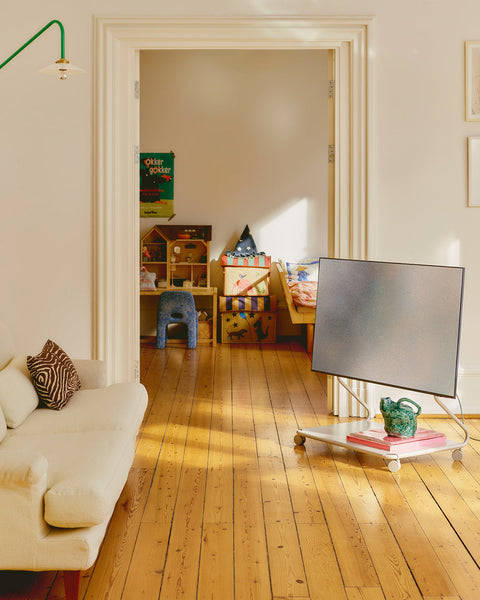 Pedestal Disco TV Stand in Oat, holding a flat screen beside a cream sofa with a doorway through to a playroom