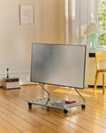 Pedestal Disco TV Stand in Chrome, low stand on wheels holding a flat screen in a bright room with a wooden floor