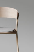 Detail of Circus Chair by EDITS, Canadian furniture brand, showcasing natural wood frame and grey seat pad.