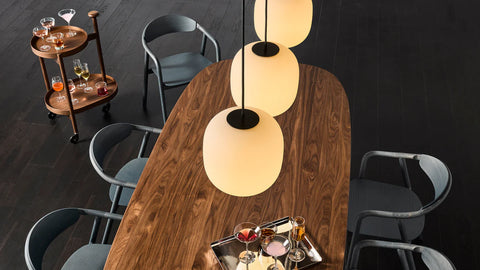Blu Dot Dibs Chairs in midnight stained beech wood, overhead view styled around a walnut dining table with white globe pendant lights and a walnut bar cart on dark hardwood floor