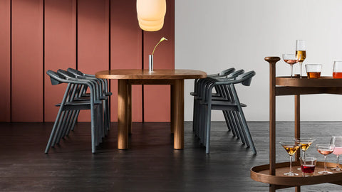 Blu Dot Dibs Chairs in midnight stained beech wood, shown stacked around a round walnut dining table demonstrating the chair's stackable design, styled with a walnut bar cart and pendant light