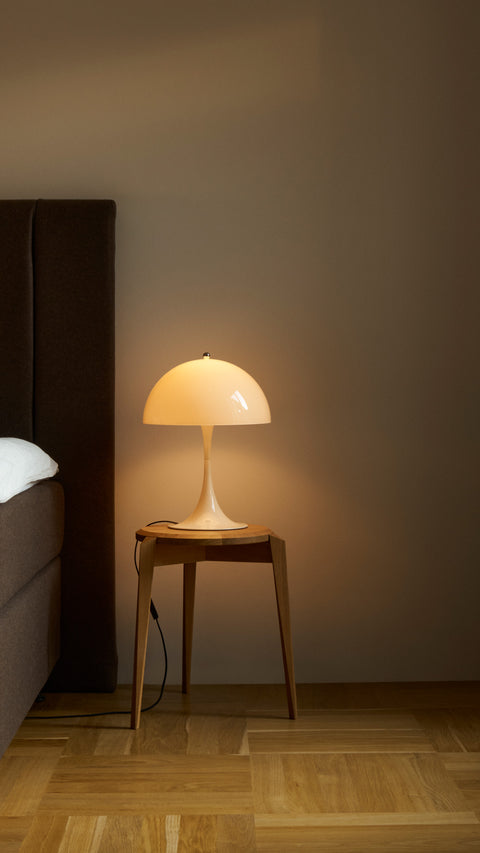 Panthella 320 Table Lamp in opal white by Louis Poulsen on a wooden bedside table, softly illuminating a cozy modern bedroom.