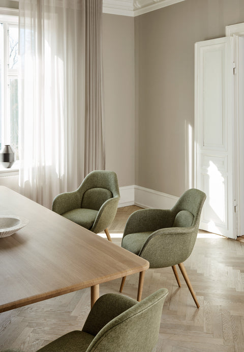 Pair of Swoon Dining Chairs with oak wood base and green fabric around a light oak dining table in a modern interior.