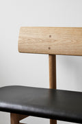 Close up of Mogensen 3171 bench showing rounded oak backrest and black leather seat detail