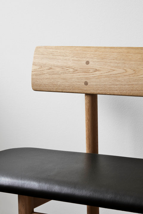 Close up of Mogensen 3171 bench showing rounded oak backrest and black leather seat detail