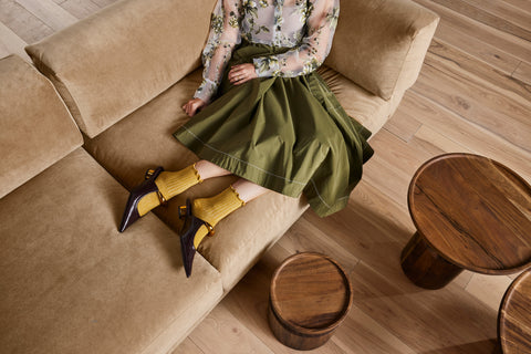 Woman in olive skirt seated on Sunday 82" Sofa by Blu Dot in Camel Velvet