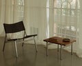 Frama Union Easy Chair, slung fabric seat on a hand brushed aluminum frame, shown beside a small wooden table at a curtained window