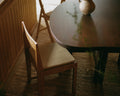 Frama Chair 01 Cushion in Camel, woven seat pad on a wooden chair pulled up to a dark round table on a woven rug