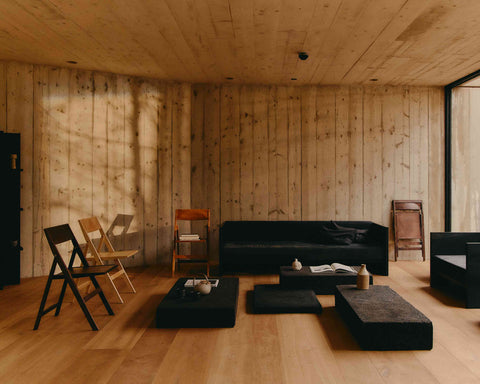 Frama Folding Flat Chair in Ash Black Birch, black folding chair by the wall of a timber lined room with a dark sofa and low tables