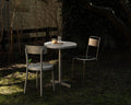 Frama Tasca Table, table with drinks and a candle between two chairs in a dark garden lit by low evening light