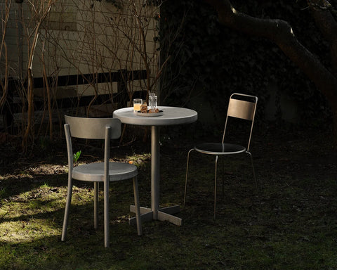 Frama Tasca Table, table with drinks and a candle between two chairs in a dark garden lit by low evening light