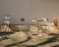Frama Petit Rond Chair in Stainless Steel, steel chairs around a small round table on a stone terrace beside a plaster wall