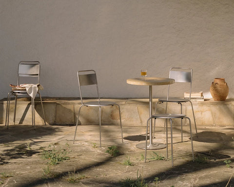 Frama Petit Rond Chair in Stainless Steel, steel chairs around a small round table on a stone terrace beside a plaster wall