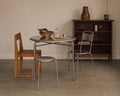 Frama Petit Rond Table, round steel table set with a bowl and carafe, flanked by a steel chair, a steel stool and a wood chair
