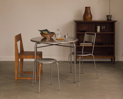 Frama Petit Rond Table, round steel table set with a bowl and carafe, flanked by a steel chair, a steel stool and a wood chair