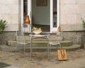 Frama Petit Rond Table, round steel table with a bowl of greens and two steel chairs on cobblestones by stone steps