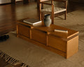 Frama Ratio Console in Warm Brown Birch, birch console on a woven rug holding a book and a stone jug, with a slatted bench behind it