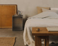 Frama Rivet Box Table in Aluminum, metal box table used at a bedside next to a cane headboard, a jute rug and a wooden bench