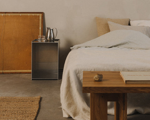 Frama Rivet Box Table in Aluminum, metal box table used at a bedside next to a cane headboard, a jute rug and a wooden bench