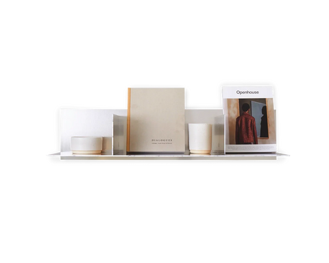 Frama Rivet Shelf, metal wall shelf lined with books, a candle, a small pot and a standing magazine against a white background