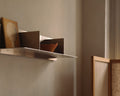 Frama Rivet Shelf, metal wall shelf holding a carved wooden panel, a divider and a small bowl in a dim warm toned room