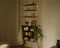 Frama Shelf Library Canvas Cabinet Section in Stainless Steel, dim kitchen corner with plates, glassware and a moka pot on the steel shelves