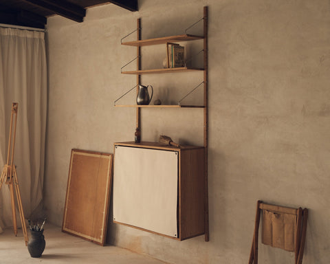 Frama Shelf Library Canvas Cabinet Section in Natural Oak, oak unit on a plaster wall, canvas fronted cabinet under shelves with a jug and books