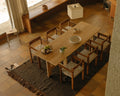 Frama Symmetry Armrest Chair in Oat Fabric and Honey Ash, six chairs around a long wooden dining table on a dark rug over a tiled floor