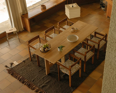 Frama Symmetry Armrest Chair in Oat Fabric and Honey Ash, six chairs around a long wooden dining table on a dark rug over a tiled floor