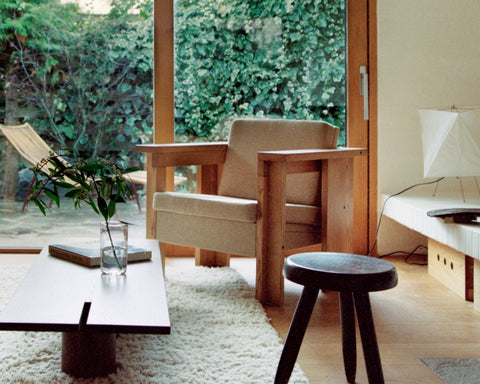 Frama Symmetry Lounge Chair in Oat Fabric and Ash, two chairs by a window with ivy outside, a low table and a dark round stool on a shaggy rug