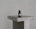 Frama T-Table in Terrazzo, table against a grey wall with a small dark glass bottle standing on the speckled slab top