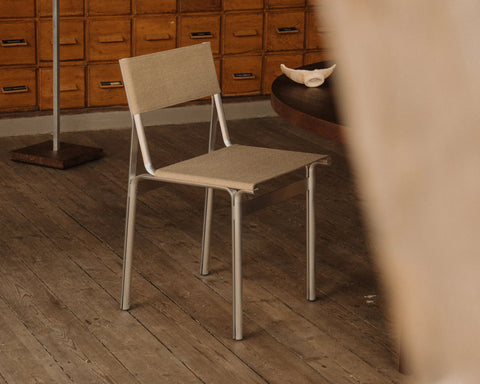 Frama Union Chair in Sandstone Linen and Aluminum, chair on a plank floor beside a counter, a wall of small wooden drawers behind