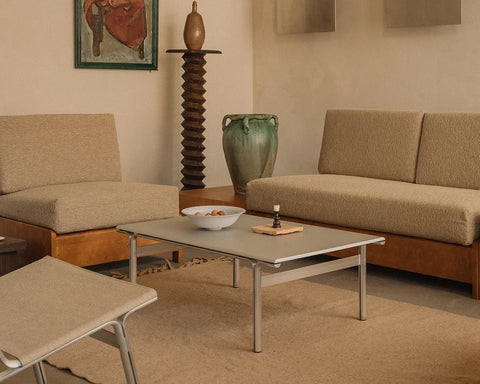 Frama Union Coffee Table in Aluminum, table with a pale top in a living room holding a bowl of fruit, upholstered seating and a green vase behind