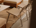 Frama Union Easy Chair in Sandstone Linen and Aluminum, two chairs on a woven rug beside upholstered seating and a low white table