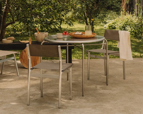 Frama Union Chair in Sandstone Mesh and Aluminum, four chairs around a round garden table laid with bowls and fruit under trees