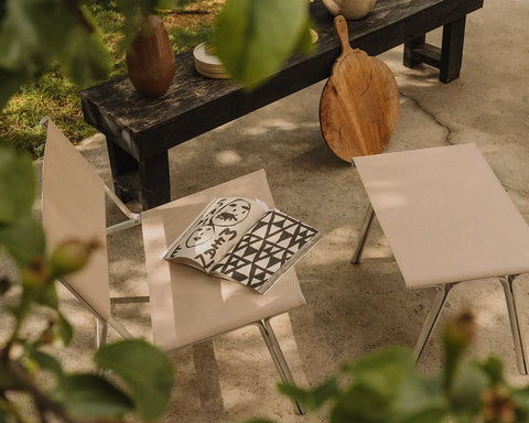 Frama Union Easy Chair in Sandstone Mesh and Aluminum, chairs on a stone terrace with an open book between them and a dark bench behind