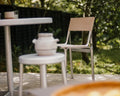 Frama Union Chair in Sandstone Mesh and Aluminum, chair outdoors beside a pale pedestal table and a stool holding a ceramic jar