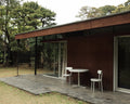 Frama Tasca Chair in Aluminum, two chairs and a small round table on the timber deck of a dark wood house among pine trees