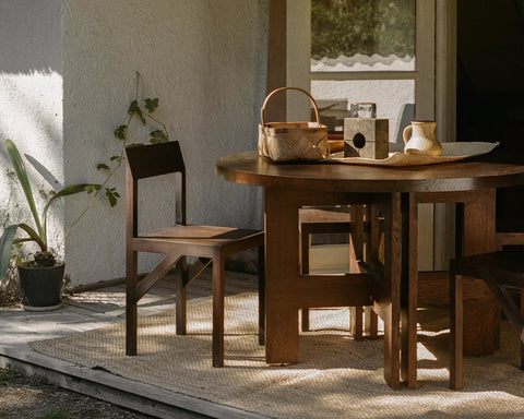 Frama Bracket Chair in Dark Brown Ash, dark ash chair on a jute rug beside a round wooden table holding a basket and a jug