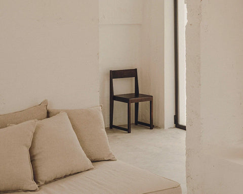Frama Chair 01 in Dark Brown Birch, dark birch chair standing in a plaster walled room beside a low beige sofa with cushions
