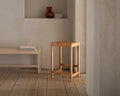Frama Stool 01 in Natural Birch, pale birch stool in a plaster room with a wall niche holding a vase and a low bench nearby
