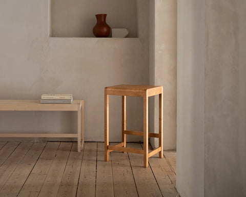 Frama Stool 01 in Natural Birch, pale birch stool in a plaster room with a wall niche holding a vase and a low bench nearby