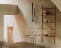 Frama Triangolo Chair in Stainless Steel, chair standing in a plaster walled room beside an oak wall shelf holding jugs and ceramics