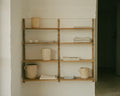 Frama Shelf Library Triple Section in Natural Oak, oak shelves on a whitewashed wall with stacked pots, folded linen and books beside a doorway