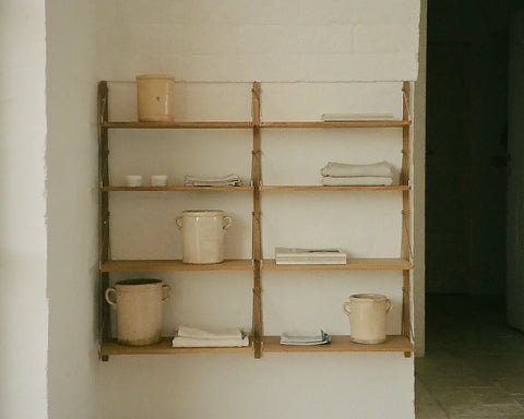 Frama Shelf Library Triple Section in Natural Oak, oak shelves on a whitewashed wall with stacked pots, folded linen and books beside a doorway
