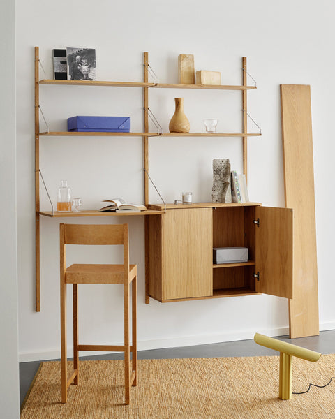 Frama Shelf Library Desk Section in natural oak styled as a home-office nook with carafe, open book, and blue archive box on the shelves