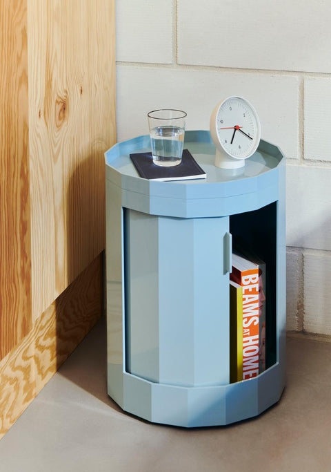 HAY Table Clock, White, white table clock, on a pale blue round cabinet with a glass of water, against a white brick wall