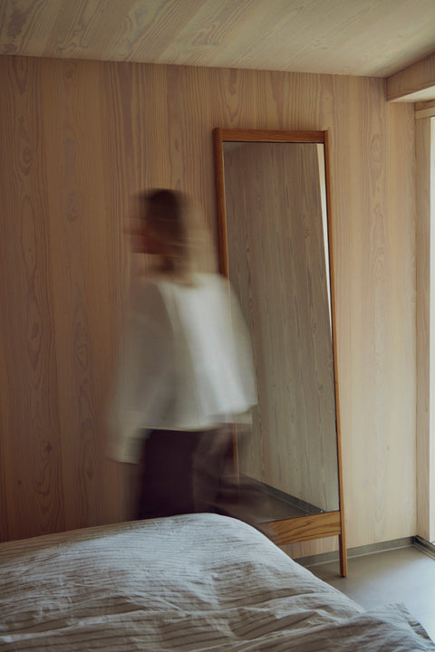 Form & Refine A Line Mirror, solid oak floor mirror, oak floor mirror leaning in a wood-panelled bedroom, a figure in white passing by