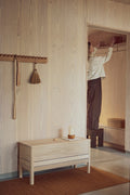 Form & Refine A Line Storage Bench 90, oak storage bench with lid, white oak storage bench beneath a coat rack in a plywood entrance, person hanging a coat